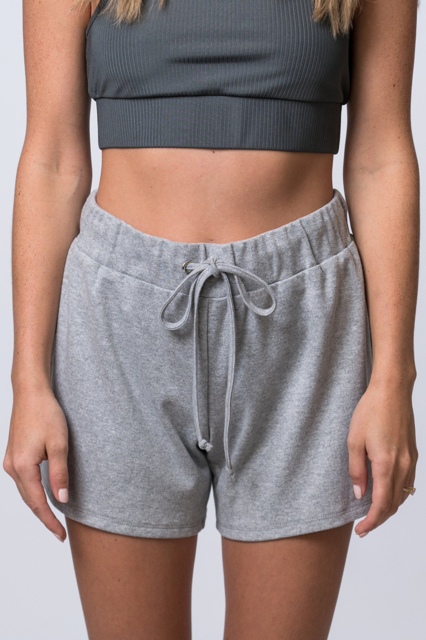 Woman wearing light gray, drawstring sweat shorts and a dark gray, ribbed sports bra. Front of clothing is being shown