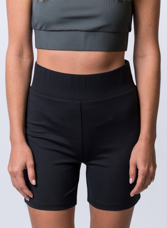 Woman wearing black biker shorts with thick waistband and a dark gray, ribbed sports bra. Front of clothing is being shown