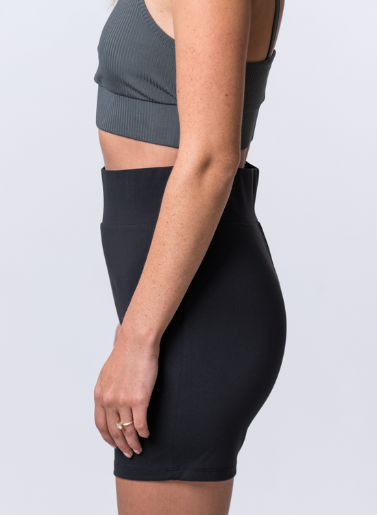 Load image into Gallery viewer, Woman wearing black biker shorts with thick waistband and a dark gray, ribbed sports bra. Side of clothing is being shown
