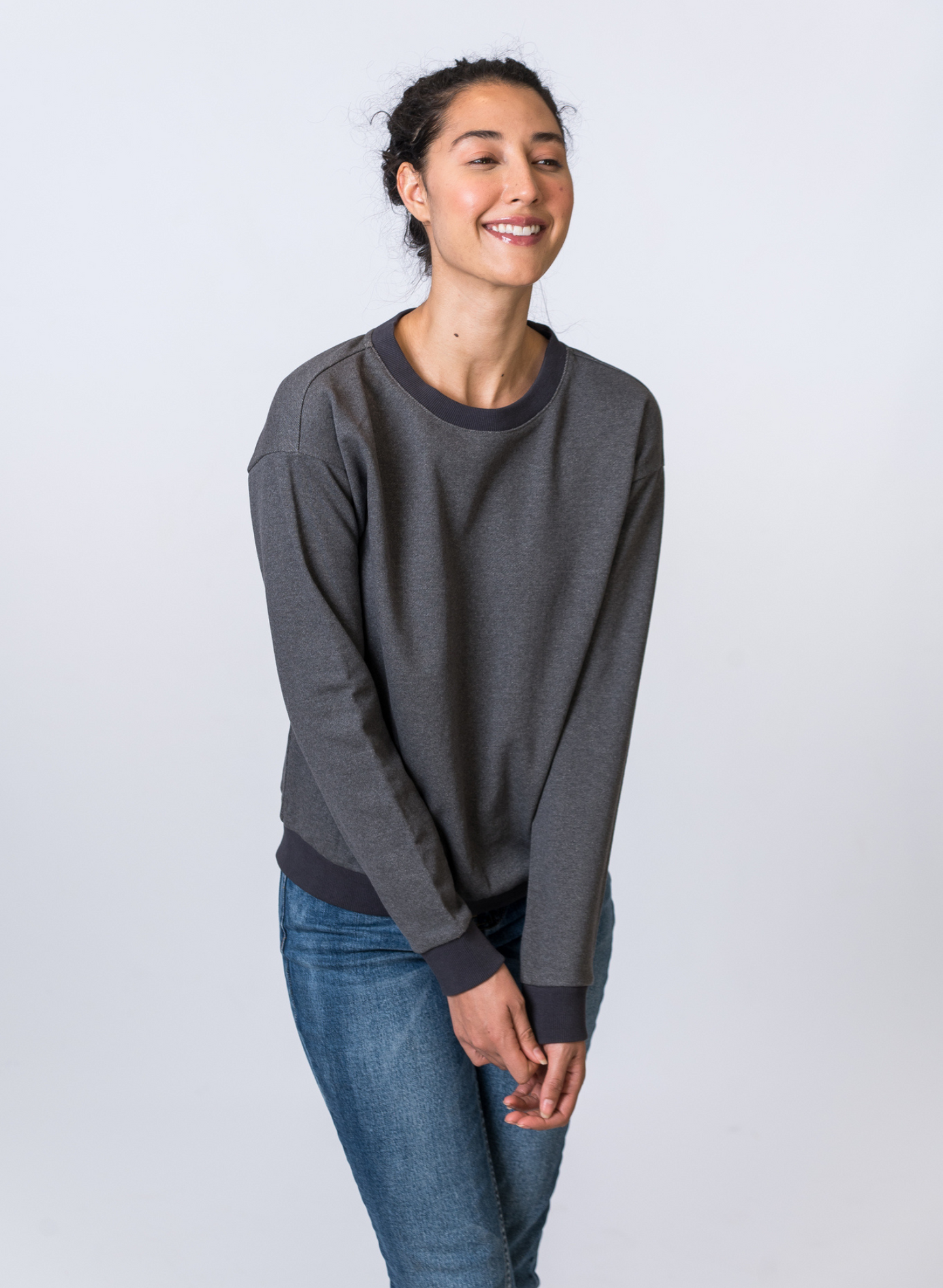 Load image into Gallery viewer, Woman smiling, wearing a dark gray crewneck with medium wash jeans. Front of clothing is being shown
