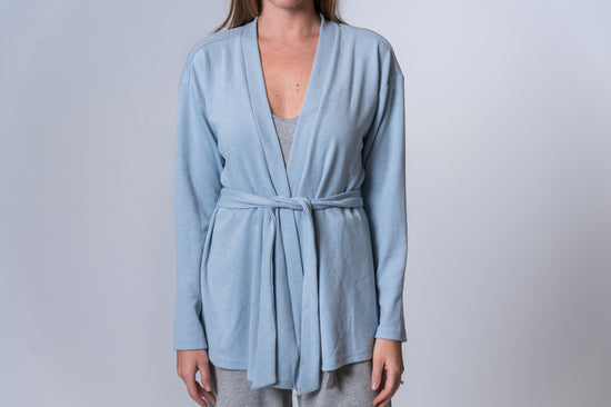 Woman wearing a light blue tie robe with gray undershirt and gray lounge pants. Front of clothing is being shown