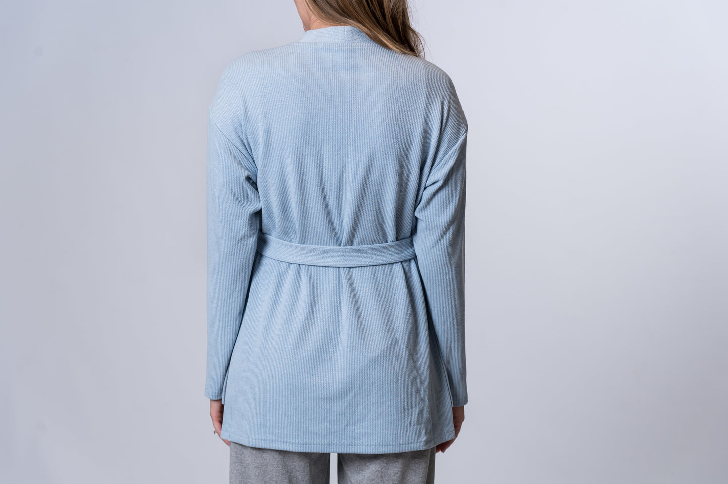 Woman wearing a light blue tie robe with gray lounge pants. Back of clothing is being shown