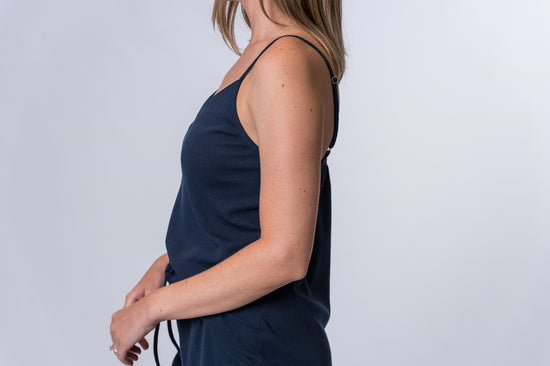 Woman wearing a dark blue tank top and matching drawstring lounge pants. Side of clothing is being shown