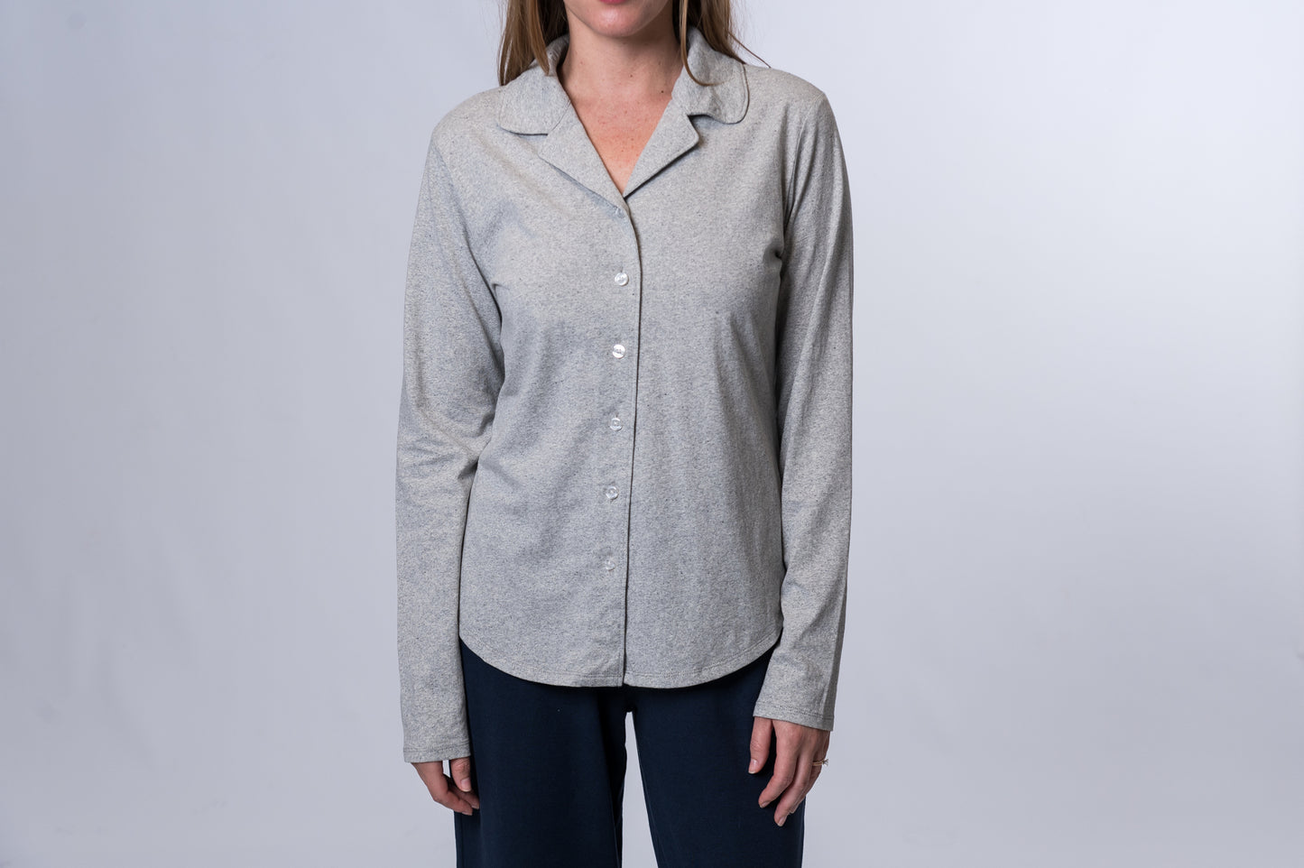 Woman wearing a light gray, long sleeve, button down sleep shirt and navy blue lounge pants. Front of clothing is being shown