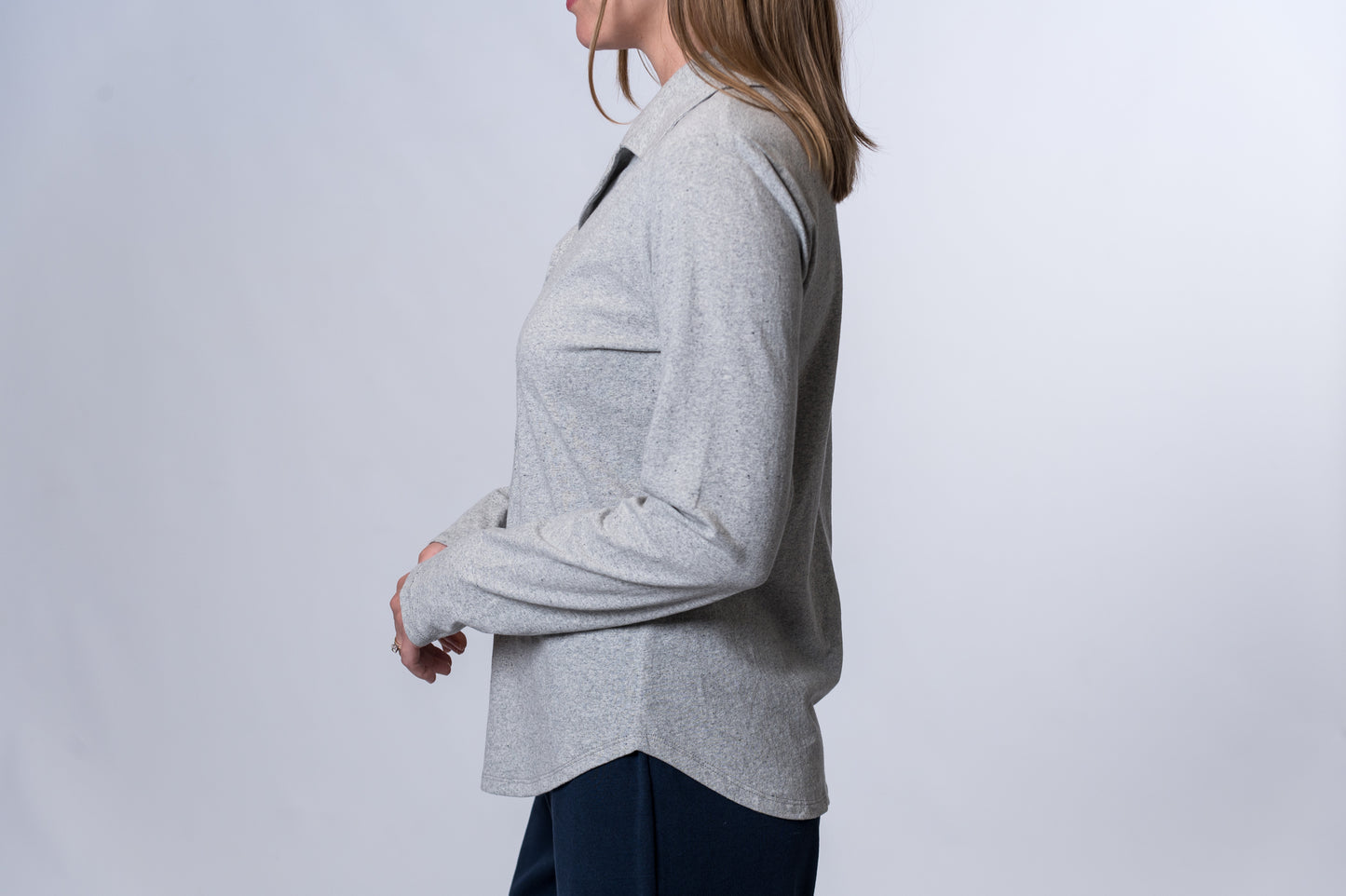 Woman wearing a light gray, long sleeve, button down sleep shirt and navy blue lounge pants. Side of clothing is being shown