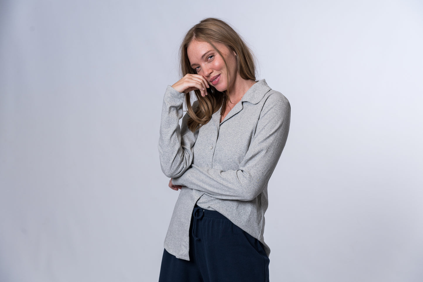 Load image into Gallery viewer, Woman wearing a light gray, long sleeve, button down sleep shirt with left side tucked into navy blue lounge pants. Front and side of clothing is being shown
