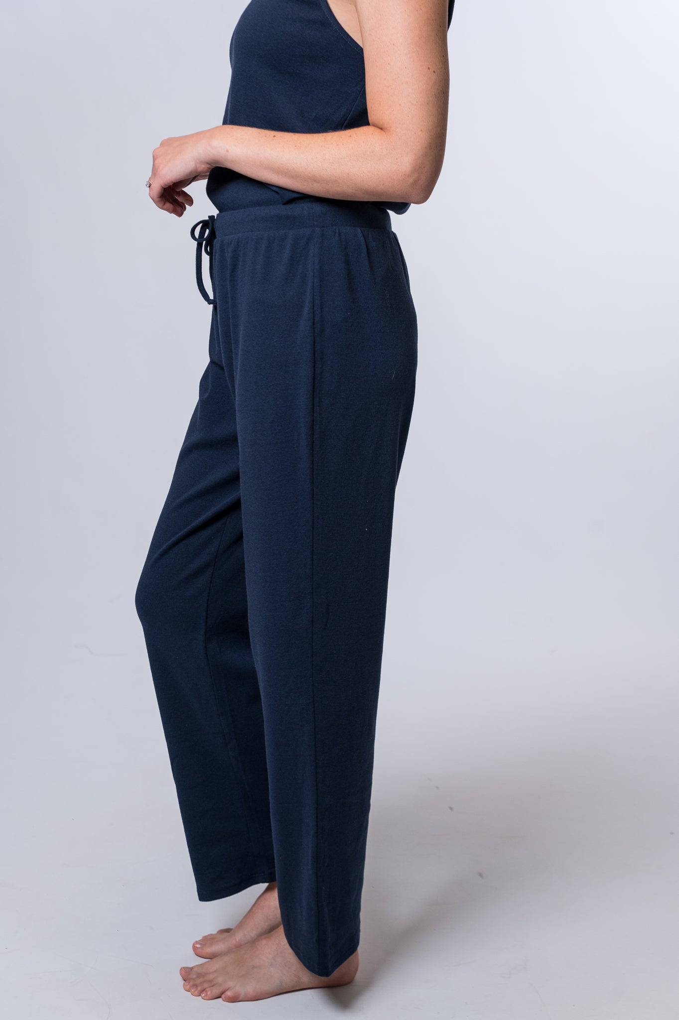 Woman wearing navy blue drawstring lounge pant and matching tank top. Side of clothing is being shown