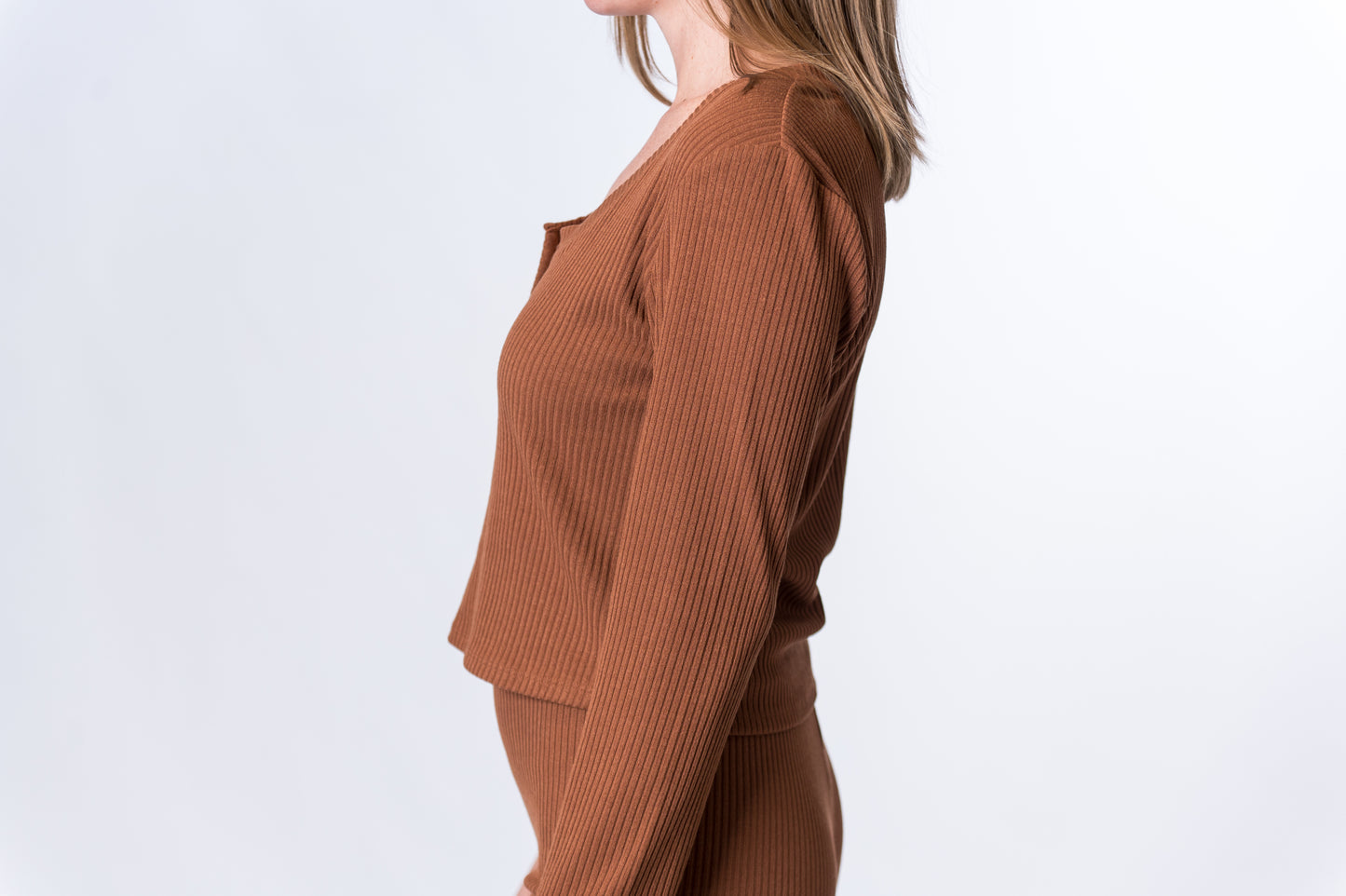 Woman wearing a brown, ribbed long sleeve lounge top with matching pants. Side of clothing is being shown