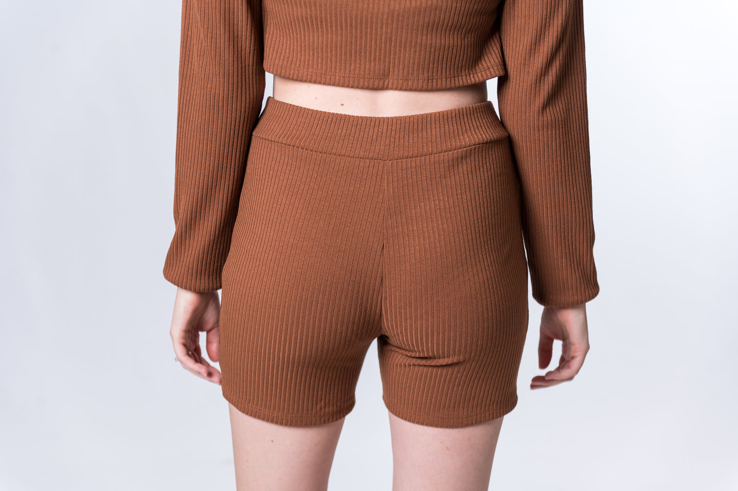 Load image into Gallery viewer, Woman wearing ribbed, brown biker shorts with matching long sleeve top. Back of clothing is being shown

