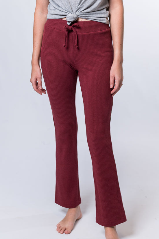 Woman wearing maroon drawstring lounge pants and a gray top with knot. Front of clothing is being shown