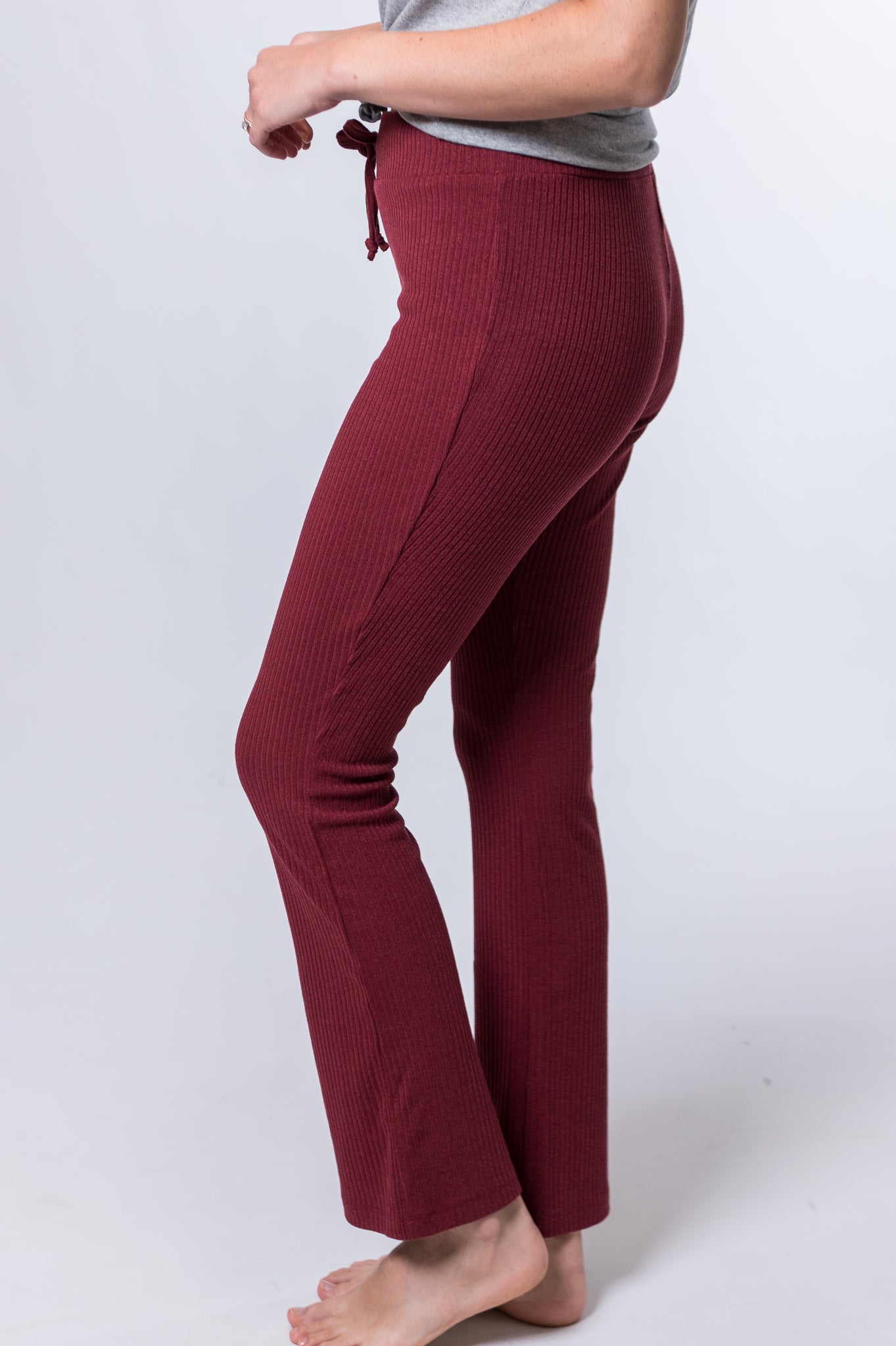 Woman wearing maroon drawstring lounge pants and a gray top with knot. Side of clothing is being shown