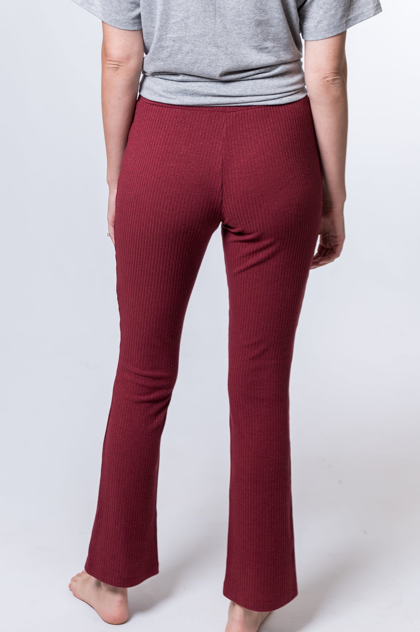 Woman wearing maroon drawstring lounge pants and a gray top. Back of clothing is being shown