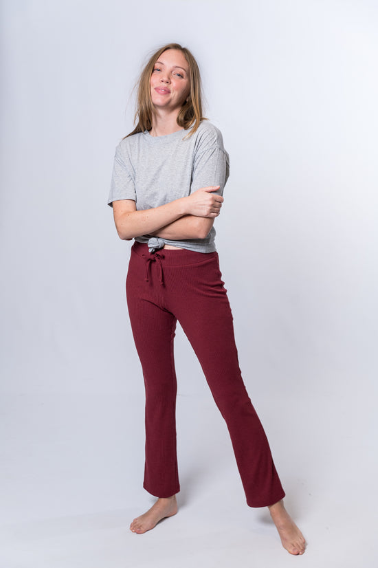 Woman crossing her arms, wearing maroon drawstring lounge pants and a gray top with knot. Front of clothing is being shown