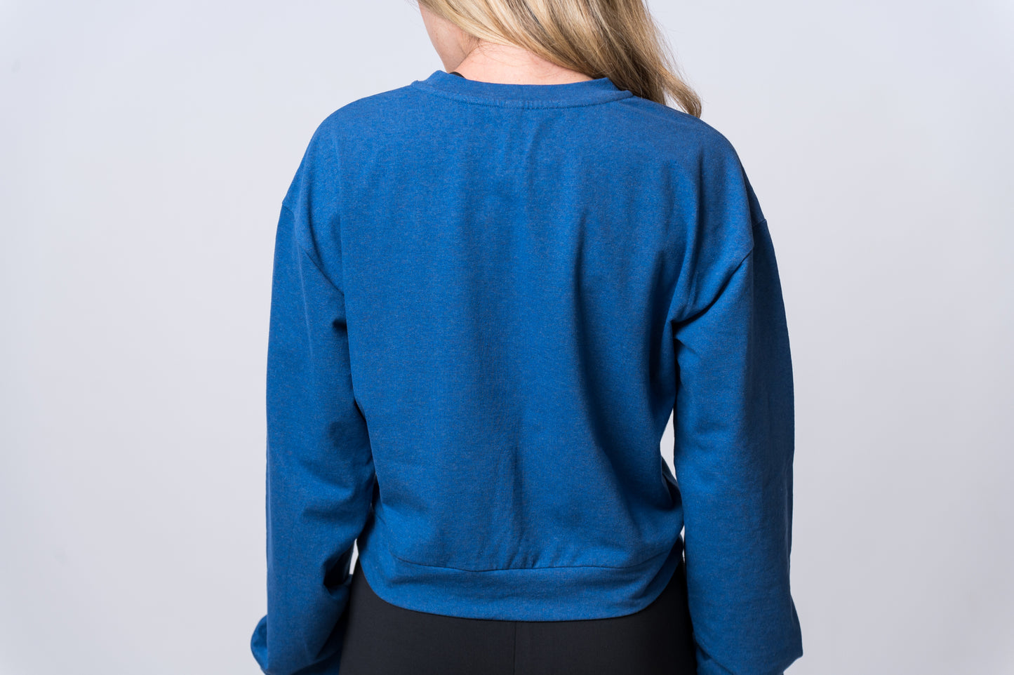 Woman wearing a blue sweatshirt with knot and black drawstring lounge pants. Back of clothing is being shown