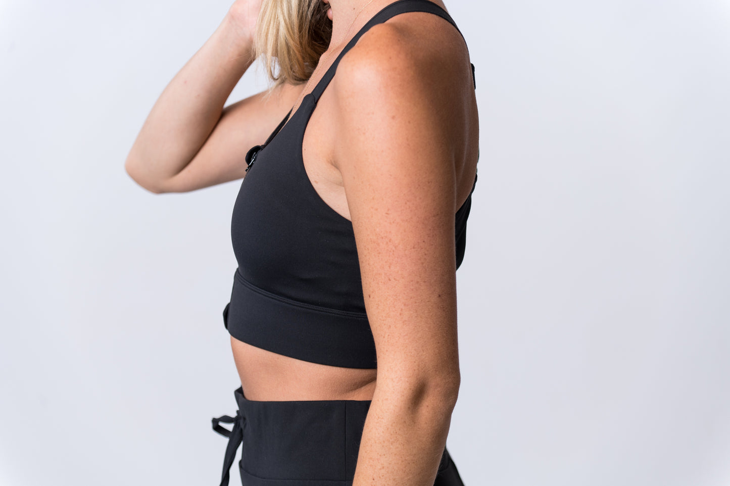 Woman wearing a black sports bra with middle zipper and black drawstring lounge pants. Side of clothing is being shown