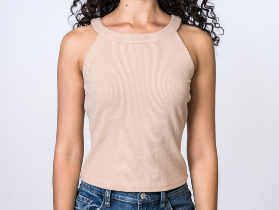 Woman wearing a tan, round neck tank top with medium wash jeans. Front of clothing is being shown