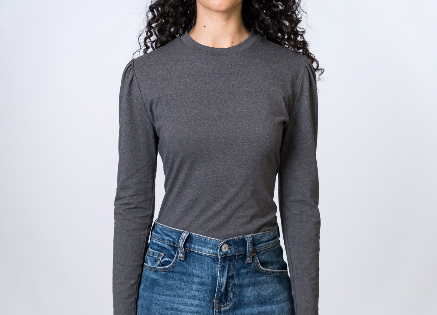 Woman wearing a gray, long sleeve top with puff sleeves and medium wash jeans. Front of clothing is being shown