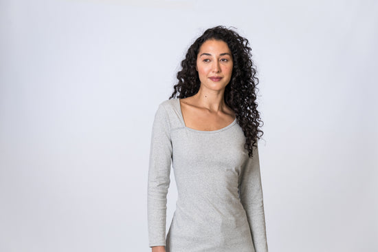 Woman wearing a light gray, asymmetric neck long sleeve top. Front of clothing is being shown