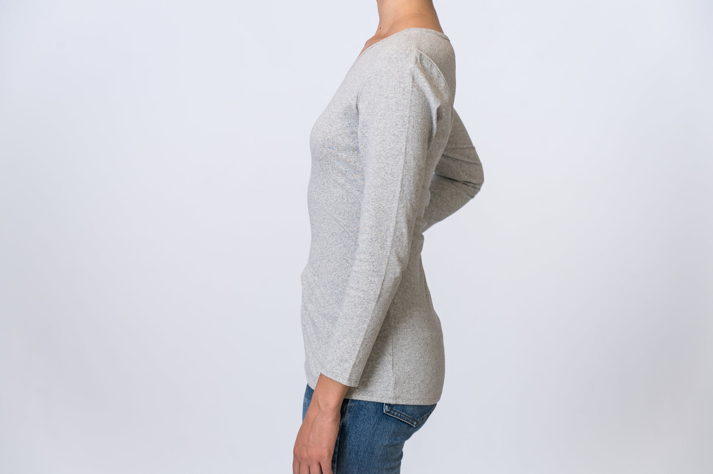 Woman wearing a light gray, asymmetric neck long sleeve top with medium wash jeans. Side of clothing is being shown