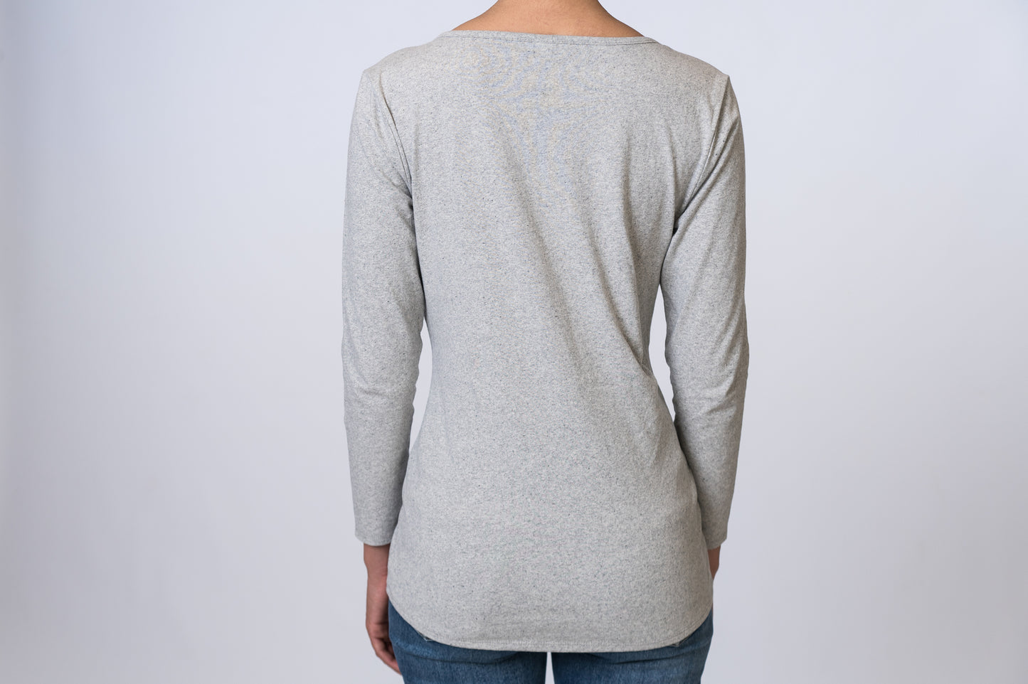 Woman wearing a light gray, asymmetric neck long sleeve top with medium wash jeans. Back of clothing is being shown