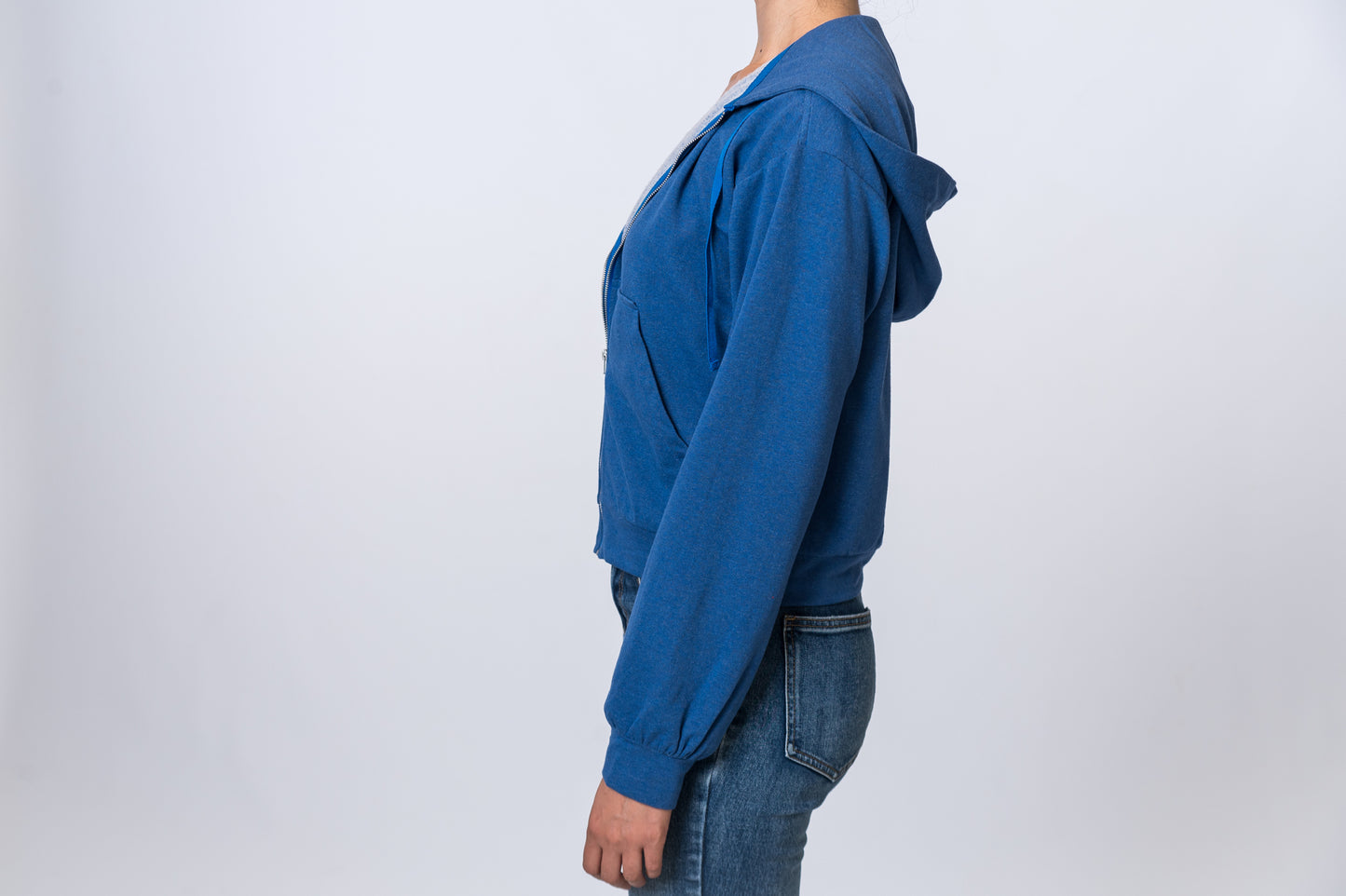 Woman wearing a blue zip up hoodie with jeans. Side of clothing is being shown