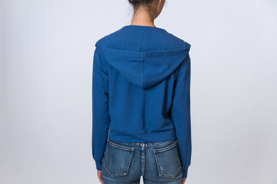 Woman wearing a blue zip up hoodie with jeans. Back of clothing is being shown