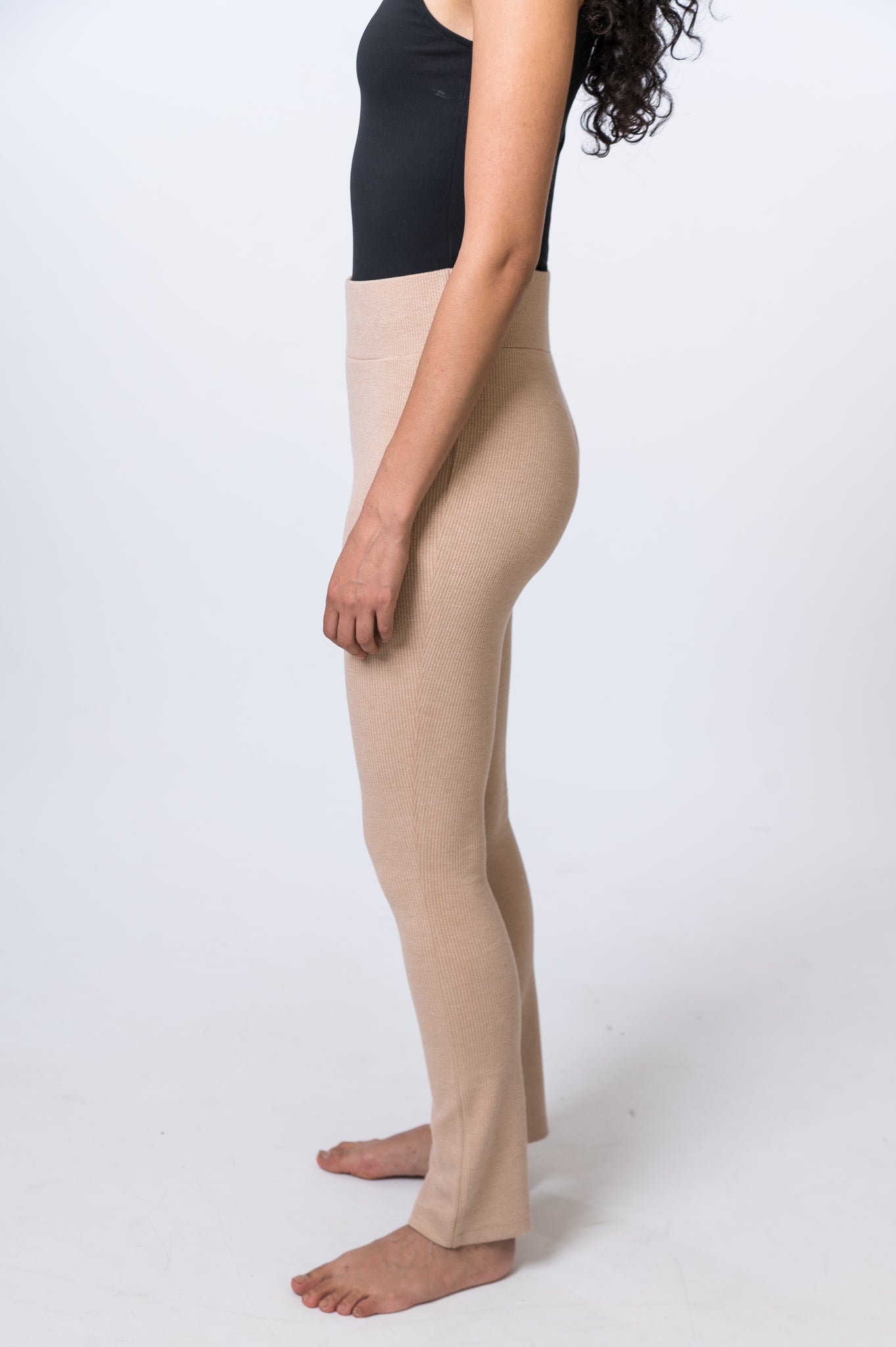 Woman wearing tan, ribbed lounge pants with a black bodysuit. Side of clothing is being shown