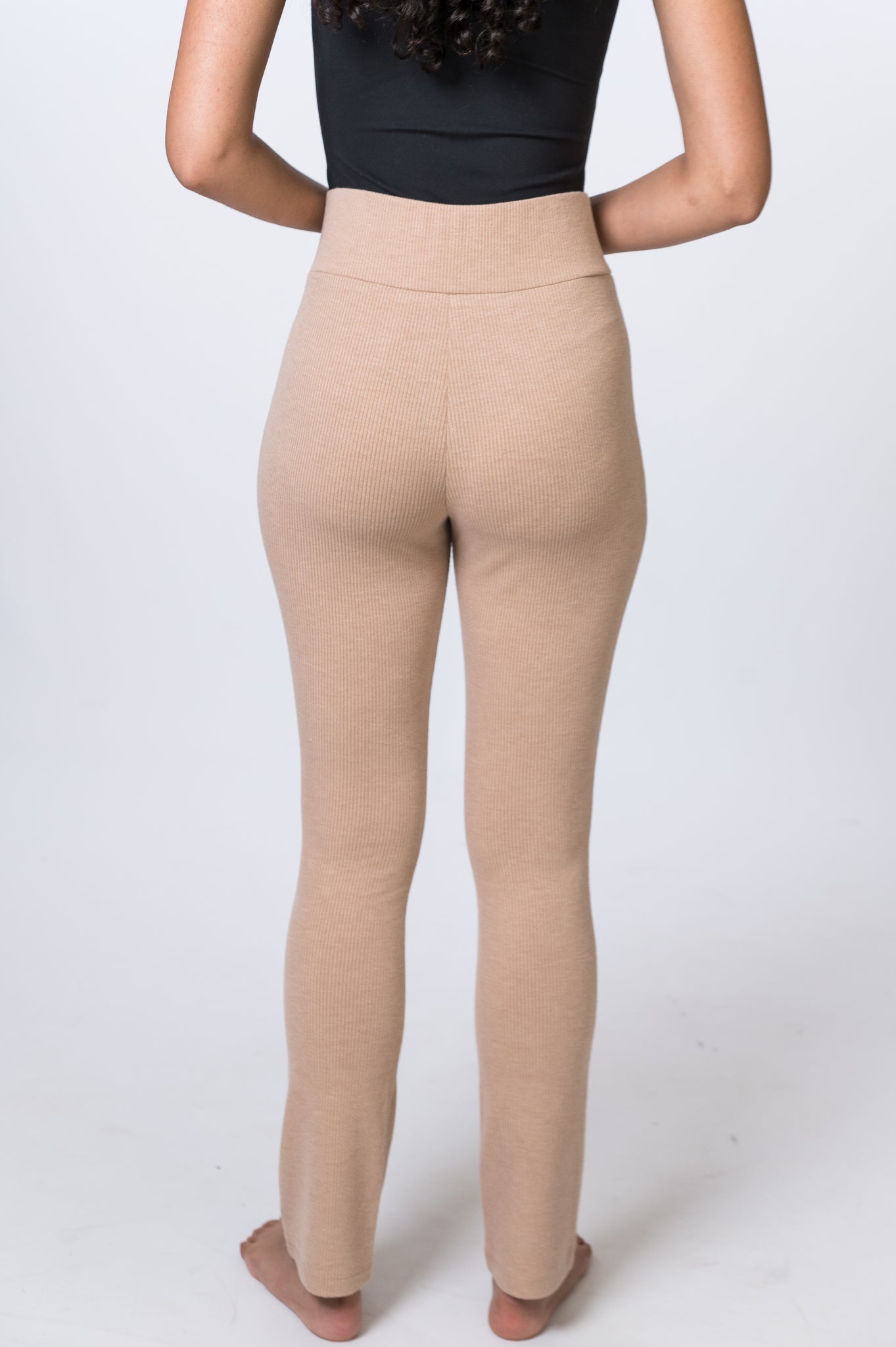 Woman wearing tan, ribbed lounge pants with a black bodysuit. Back of clothing is being shown