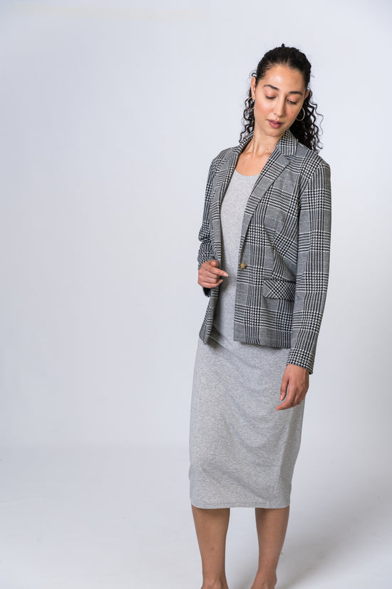 Woman wearing a light gray midi dress with a black and white striped blazer. Front and side of clothing is being shown