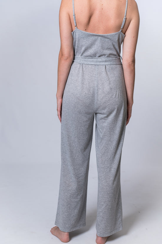 Load image into Gallery viewer, Woman wearing a light gray jumpsuit with tie belt. Back of jumpsuit is being shown
